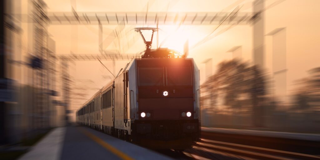 Passenger train fast passing through railroad station. Railway at sunrise with blur effect.