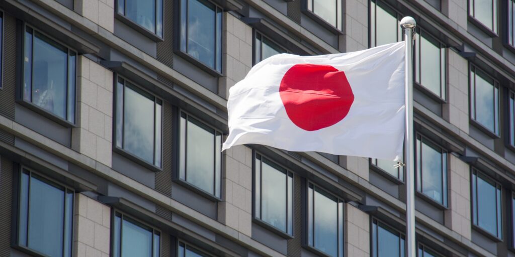 Low angle shot of the flag of Japan waving in the wind in front of the buildings on a sunny day